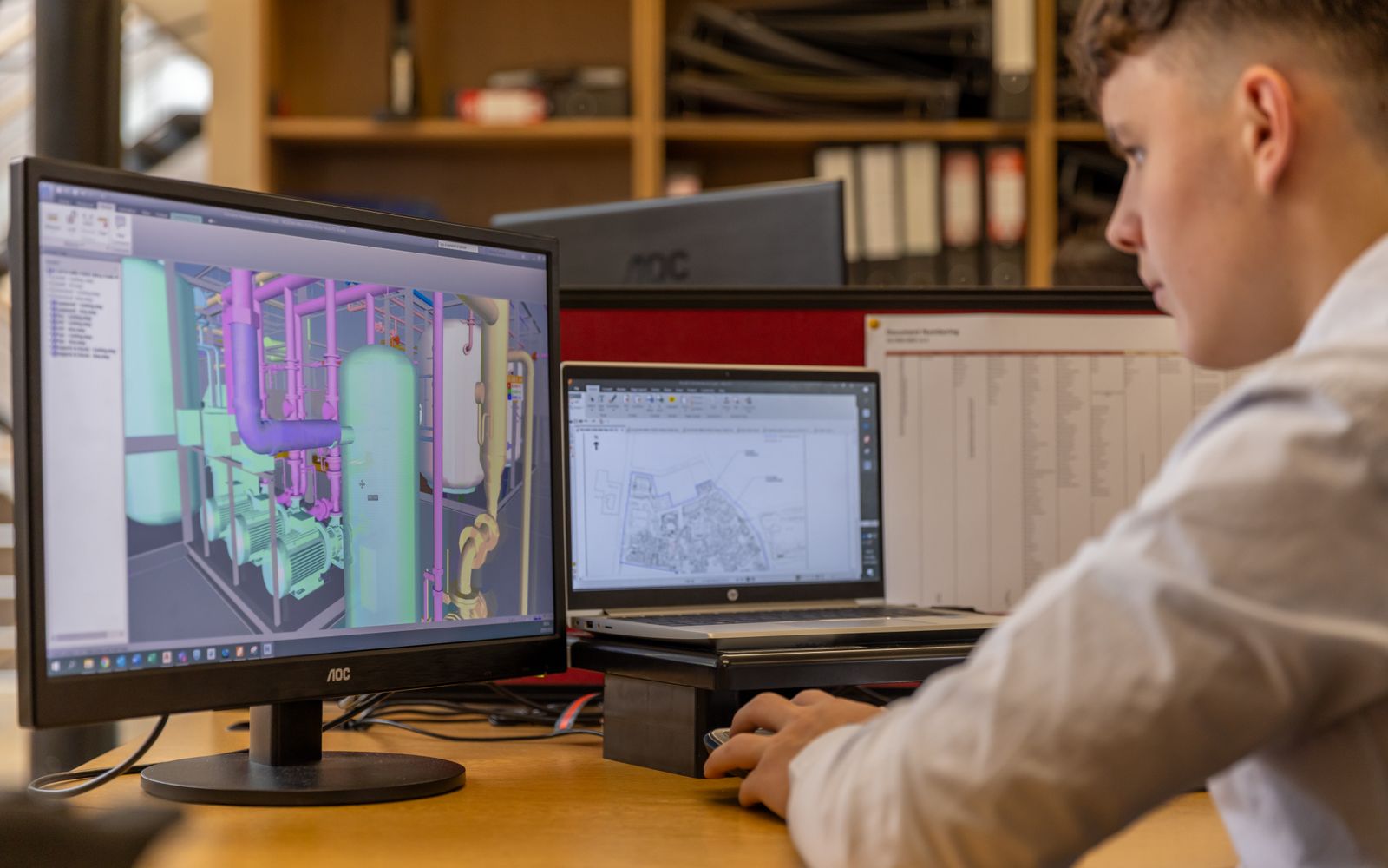 Engineer working with CAD software on dual monitors in an office setting.