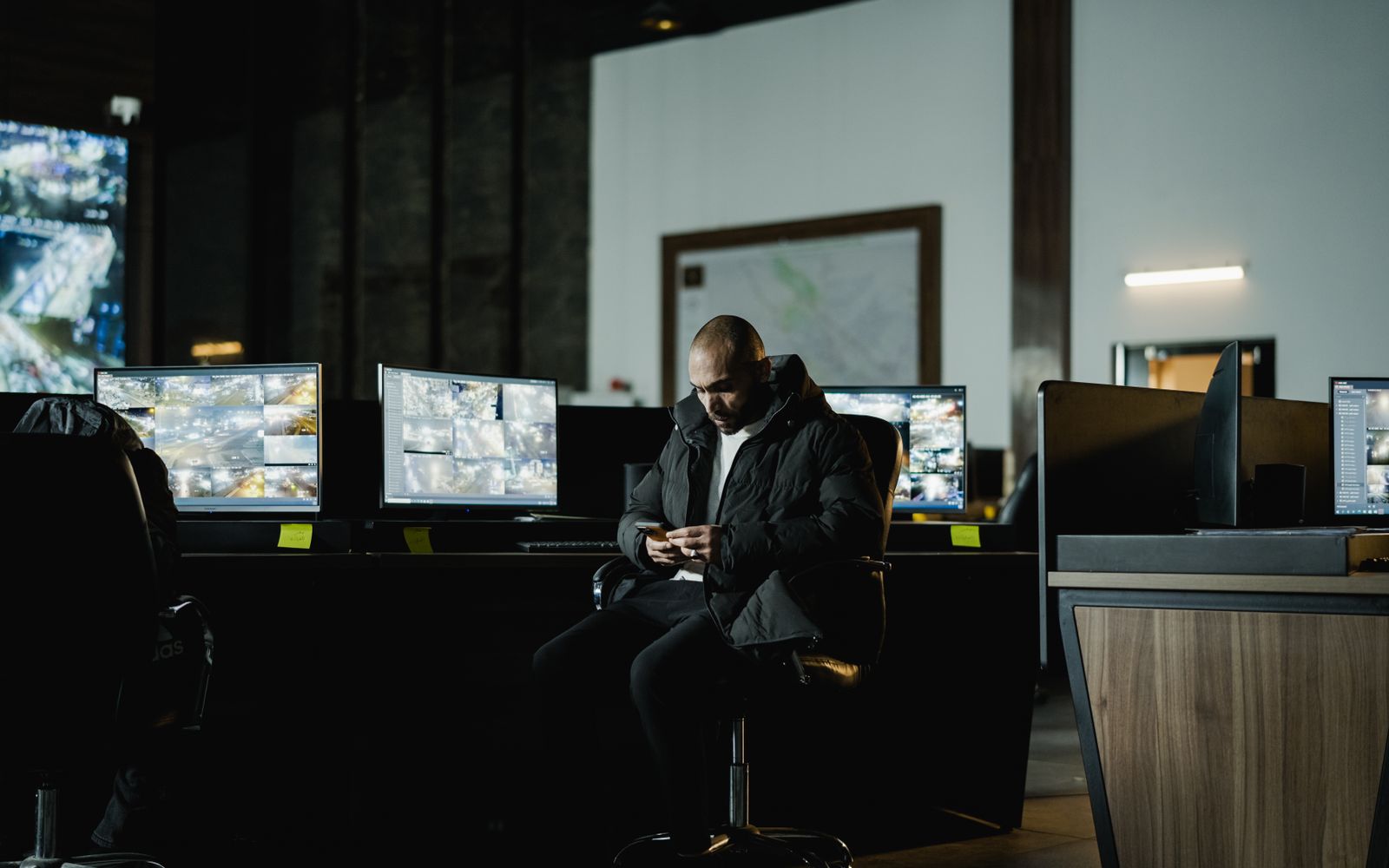 Security officer seated in a dimly lit control room, analyzing multiple surveillance screens.