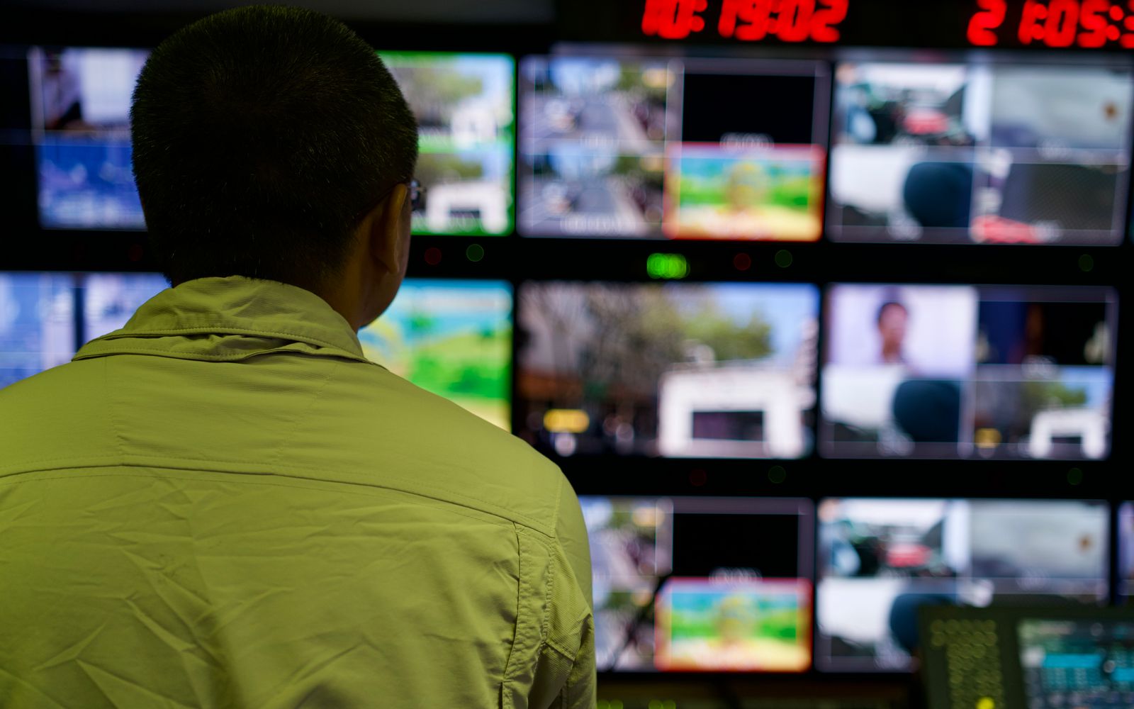 Man in a control room overseeing multiple monitors displaying various scenes.
