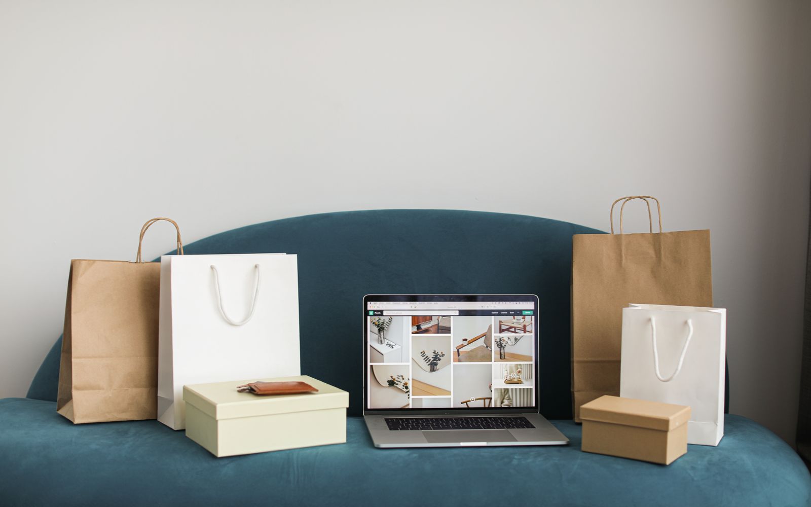 A laptop surrounded by shopping bags and boxes on a blue sofa, ideal for online shopping themes.