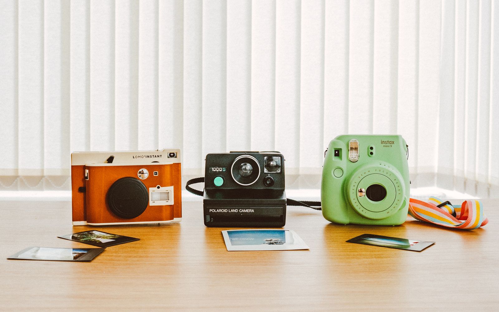 A collection of vintage and instant cameras on a wooden table with printed photos.