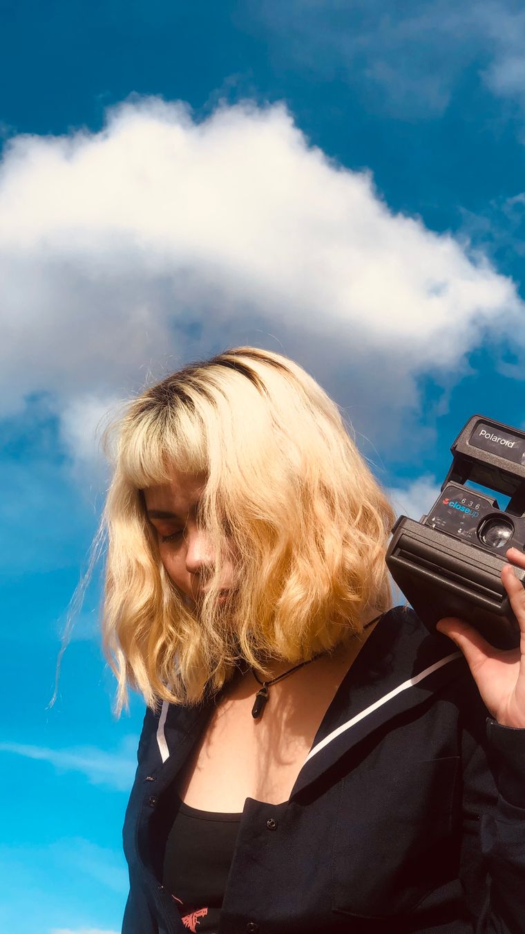 Young ethnic female standing with retro camera in hands in daytime under blue cloudy sky