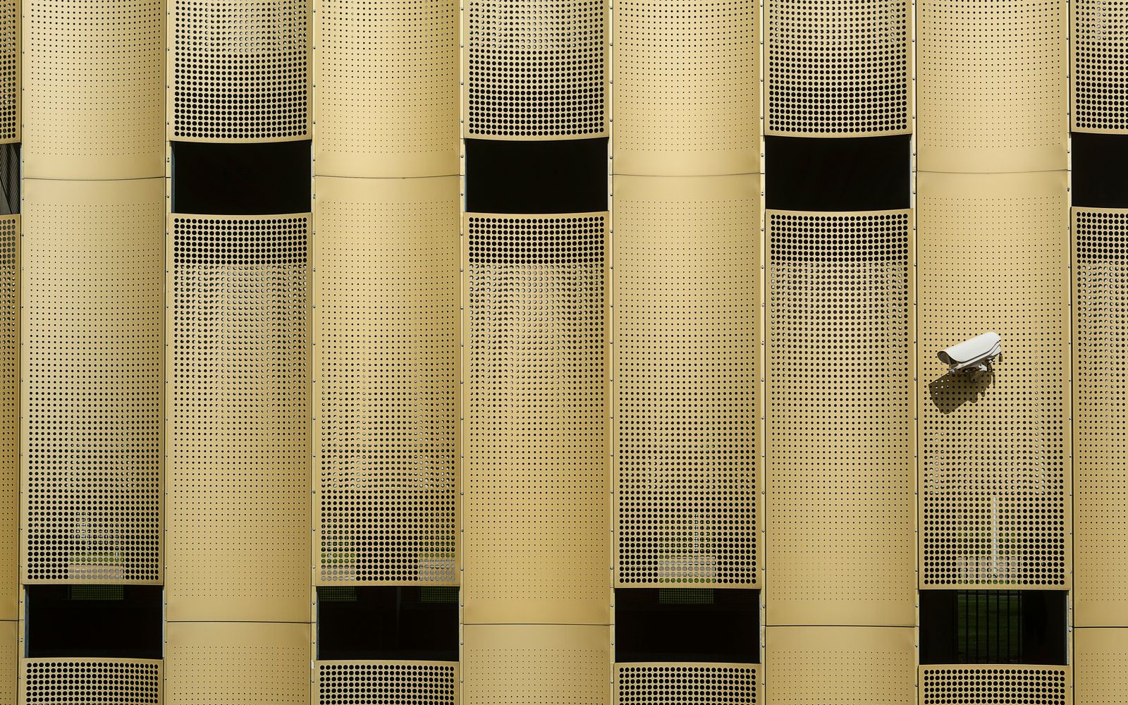 Close-up of a modern building facade with a prominent CCTV camera, showcasing architectural design.