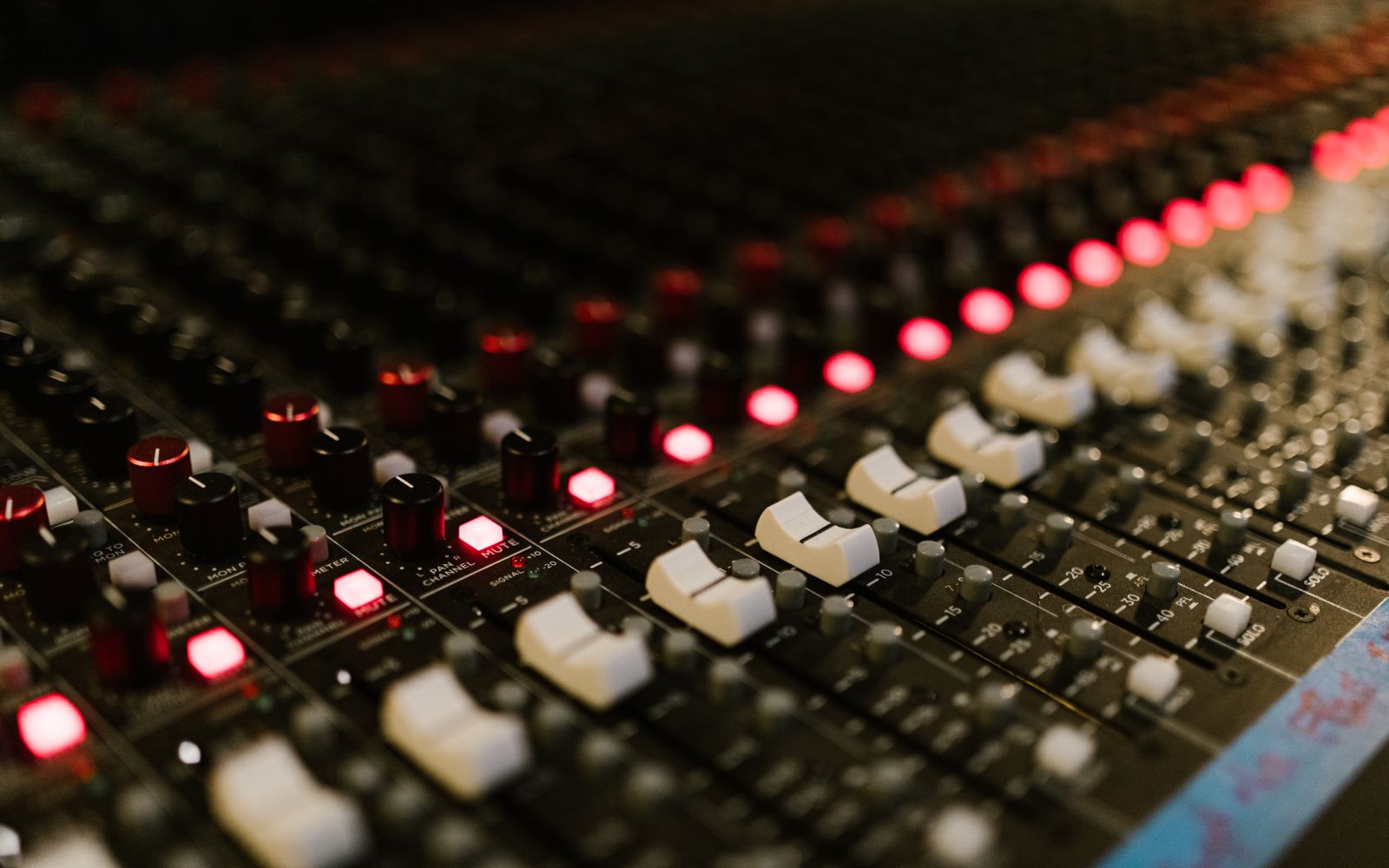 Close-up of a sound mixing console with illuminated control knobs in a music studio.