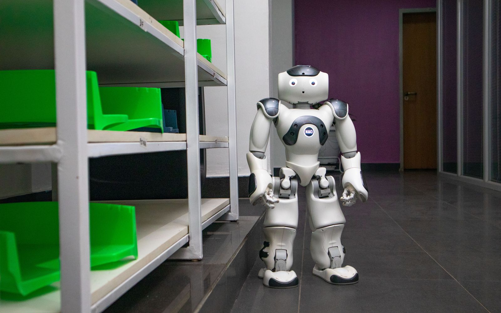 A humanoid robot standing in a modern corridor with shelves, representing futuristic technology.