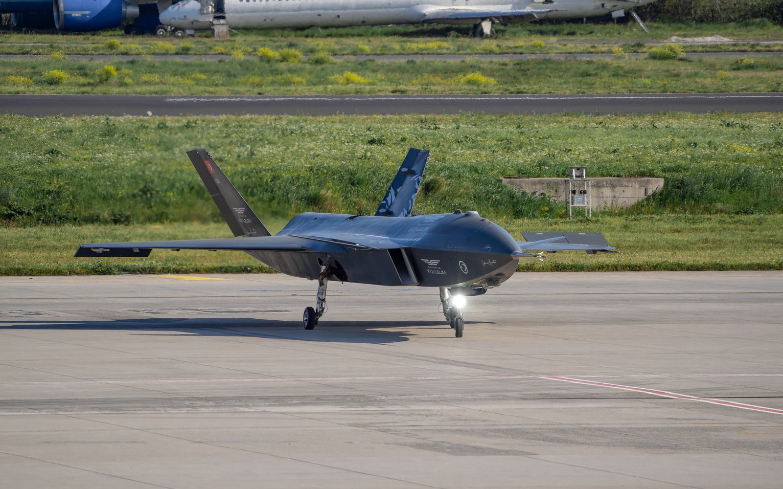 Turkish Baykar Bayraktar Kizilelma drone on a tarmac in Istanbul with aircraft in the background.