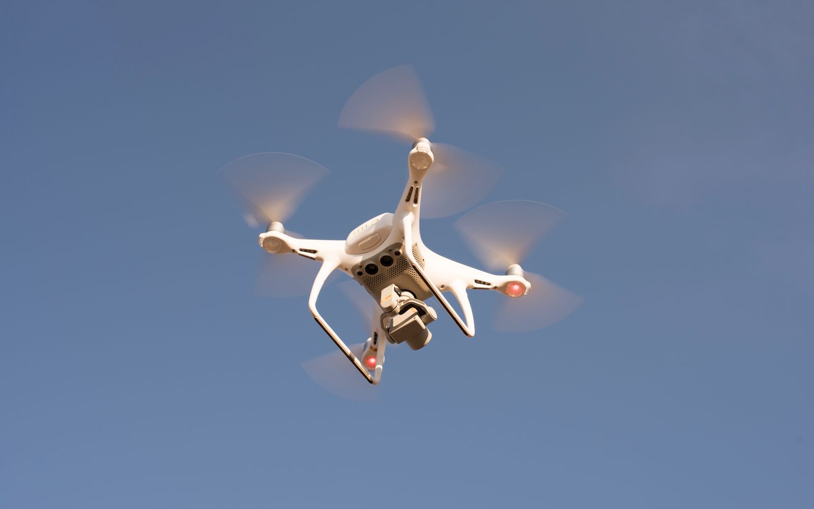 A white drone in flight against a clear blue sky, capturing aerial footage with precision.