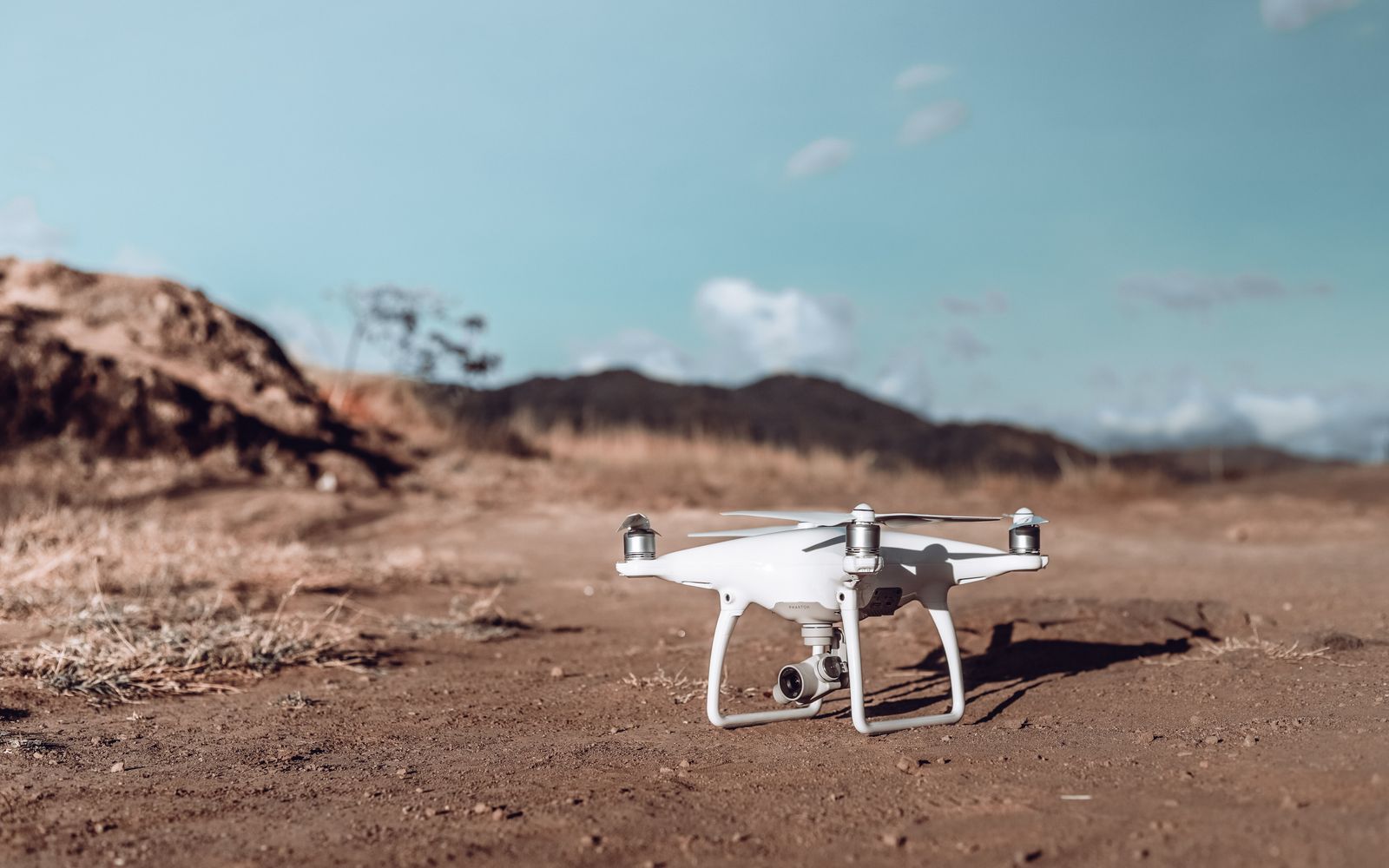 White drone ready for takeoff on a rugged desert landscape under a clear blue sky.