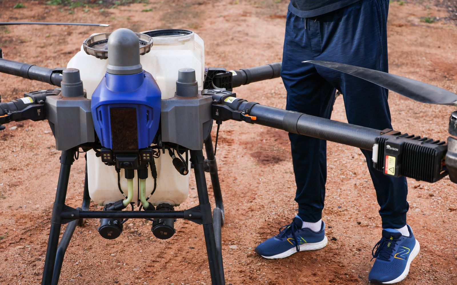 Close-up of an agricultural drone in use on a dirt field, piloted by a person.