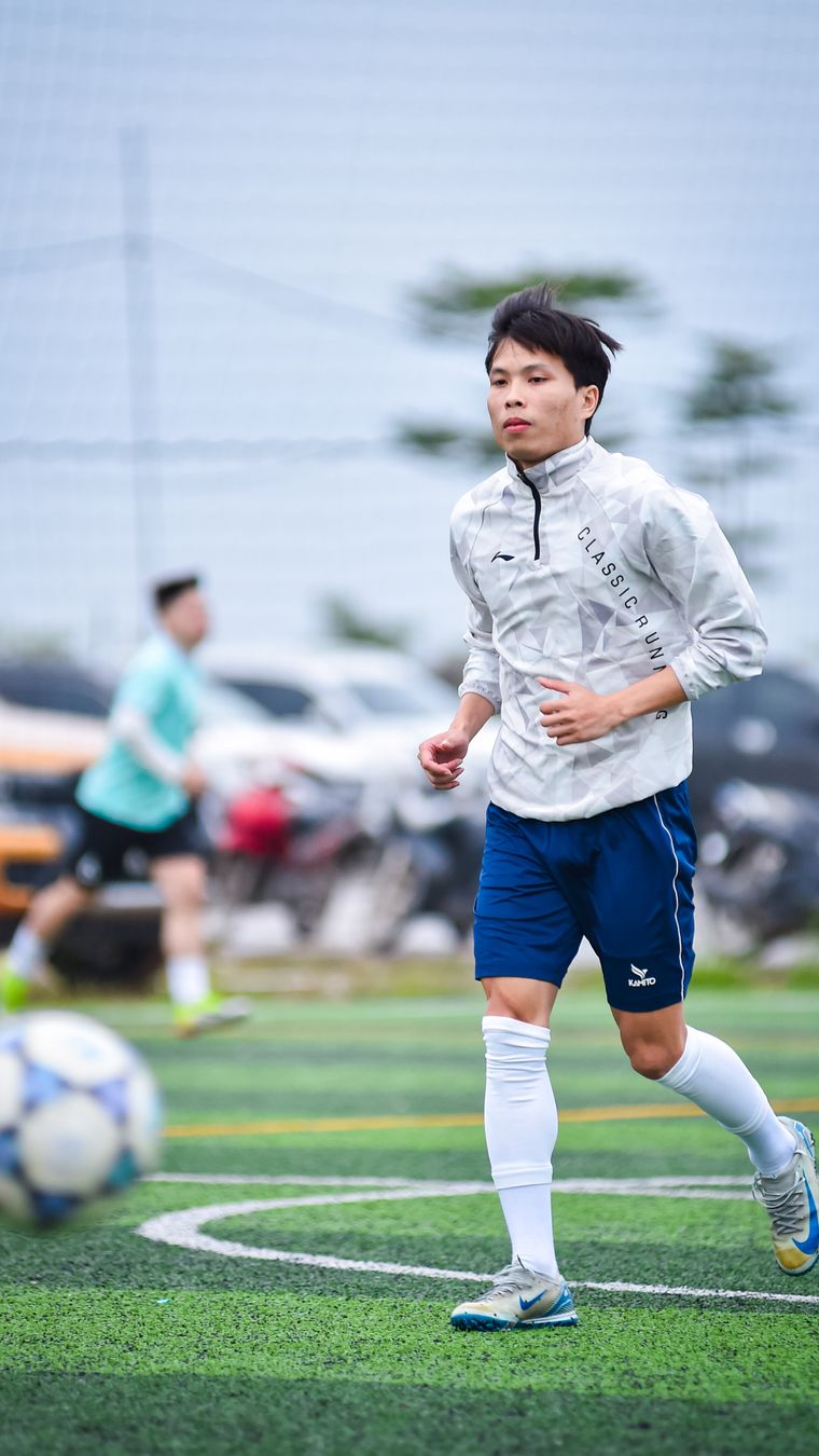 Dynamic shot of a young man playing soccer on an artificial turf field in Hà Nội, Việt Nam.