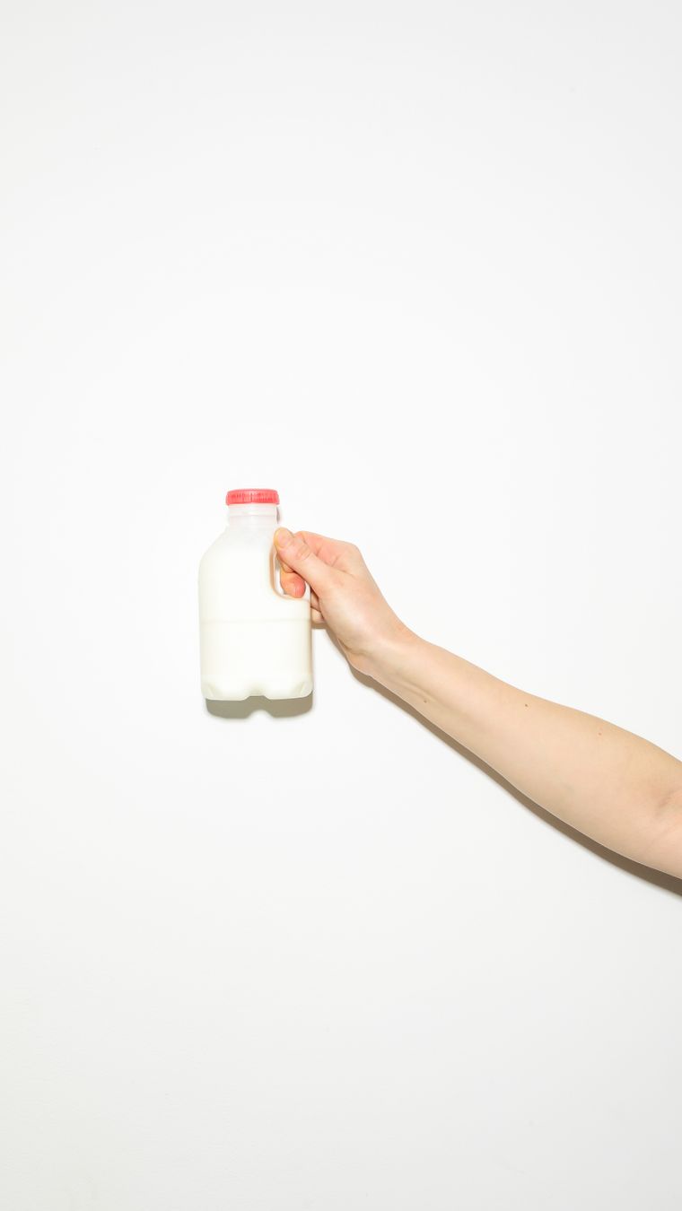 A clean, minimalist image of a hand holding a milk bottle, emphasizing freshness and simplicity.