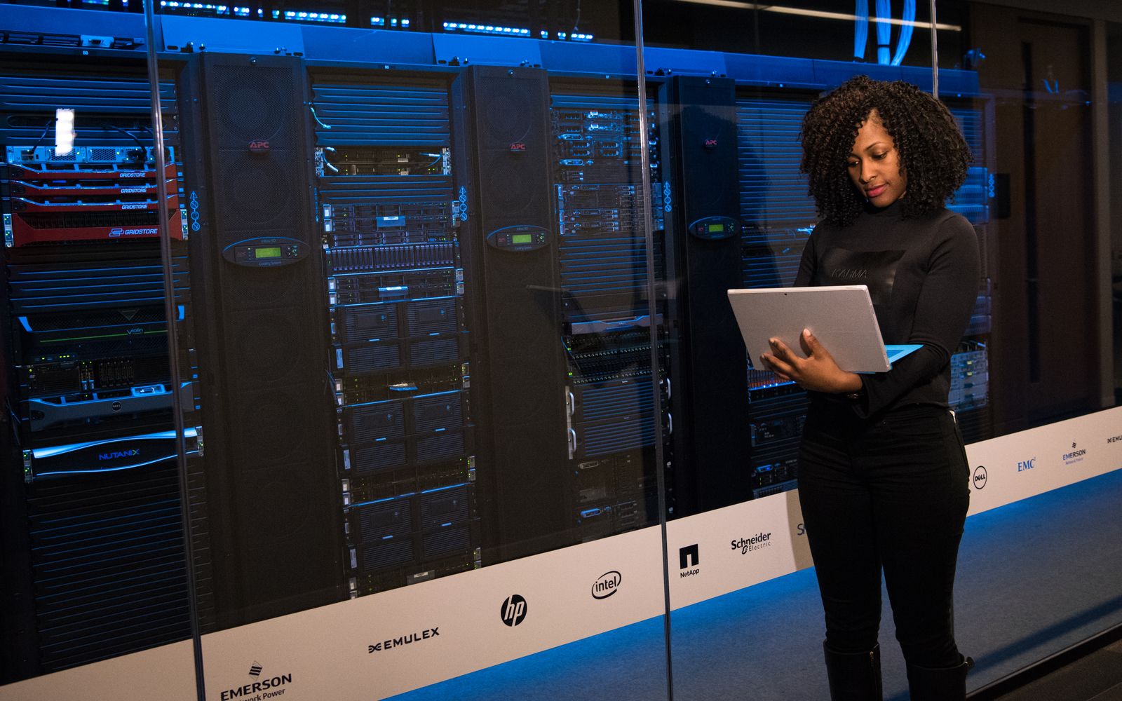 A female engineer using a laptop while monitoring data servers in a modern server room.