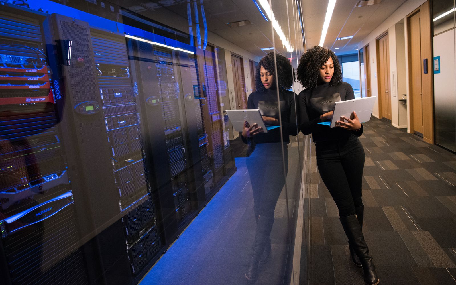 A woman using a laptop navigating a contemporary data center with mirrored servers.