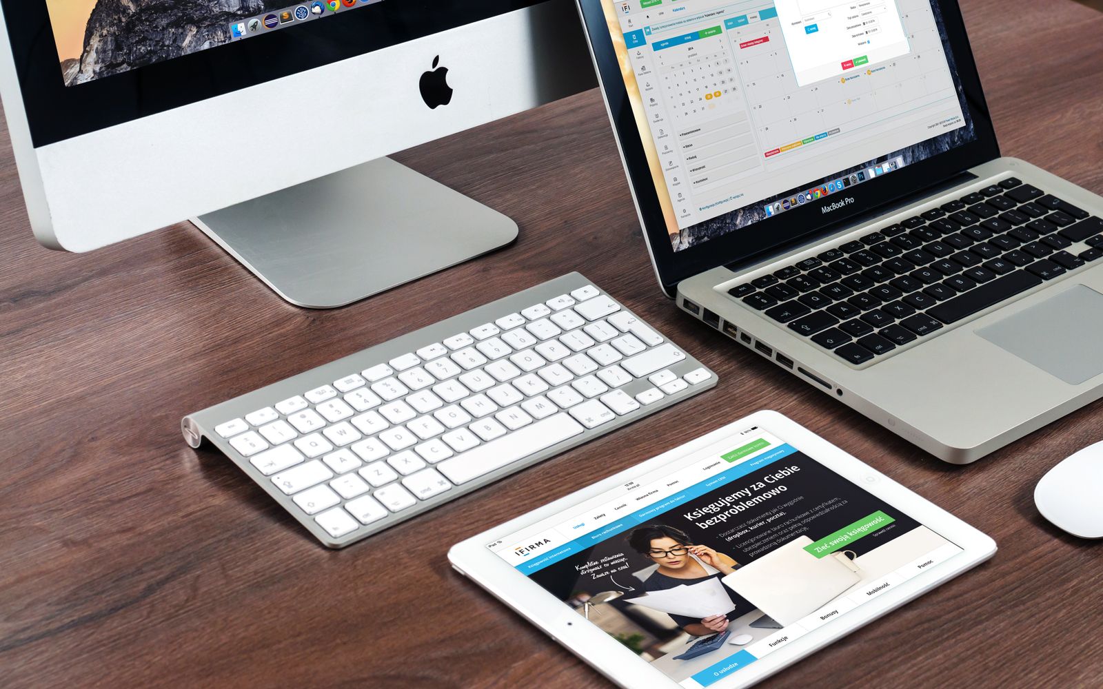 A sleek office desk setup featuring Apple devices: iMac, MacBook, and iPad.